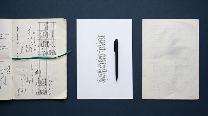 A printed course outline lies open on a desk in daylight beside a marked class quiz turned face down, a sheet of plain paper between them carrying a short column of handwritten sums.